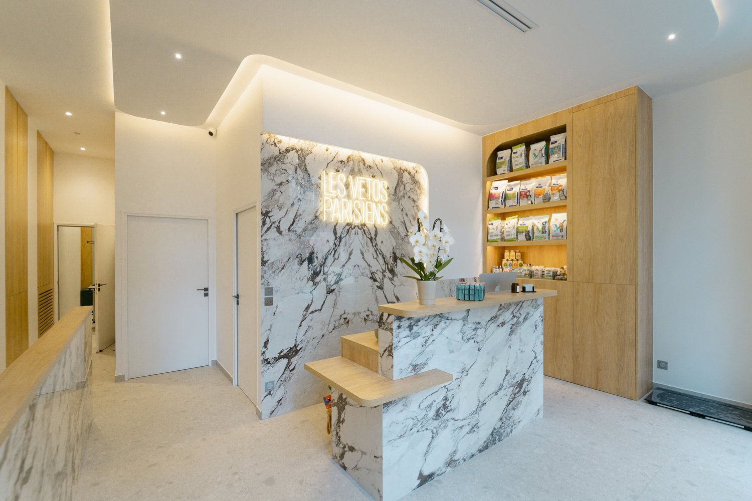 Intérieur chaleureux de la clinique : comptoir en marbre et étagères en bois clair.
